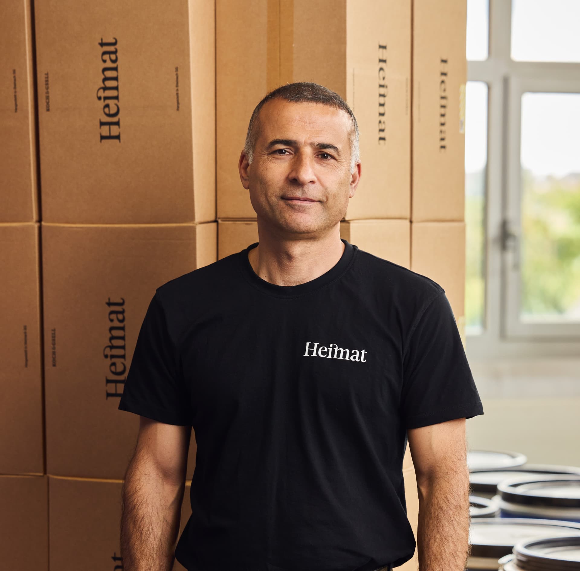 Bülent in the Heimat warehouse in front of stacks of Heimat cartons